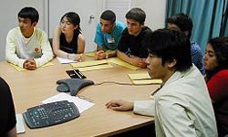 Students at table listen to Joe Kolecki via video conference.
